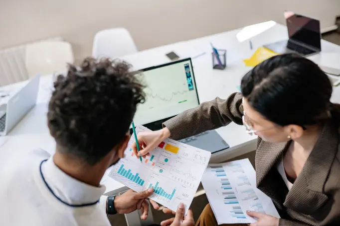 Two colleagues in an office reviewing performance charts and a dashboard together