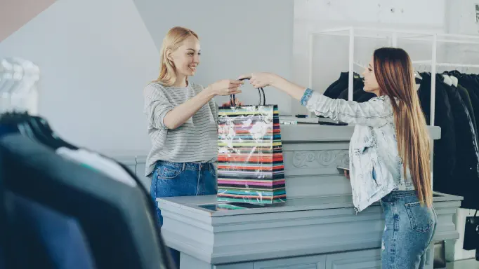 A retail store checkout, an assistant handing a customer their shopping bag