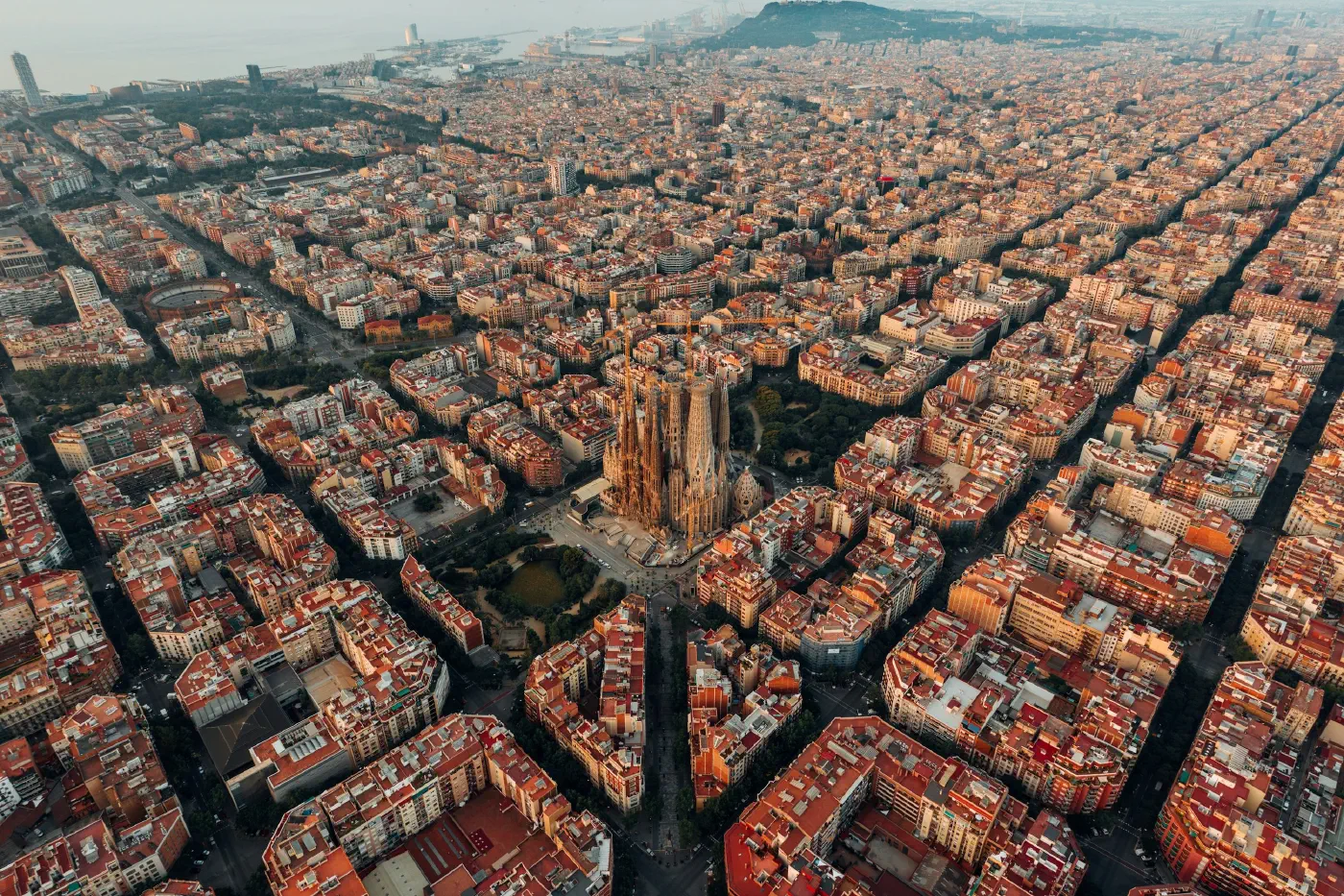 Aerial view over Barcelona's Eixample, a dense, orderly grid of city blocks around the Sagrada Familia, the readable structure a store decision actually sits in.