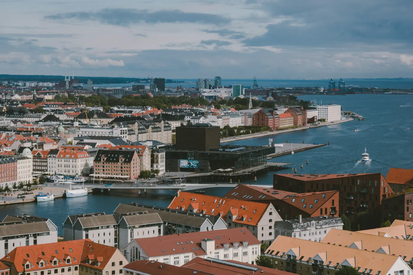 Aerial view over central Copenhagen, waterfront, red-tiled roofs and streets, the residents and local signals a forecast reads.